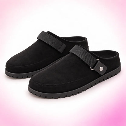 Black strappy clogs on a blush pink studio background
