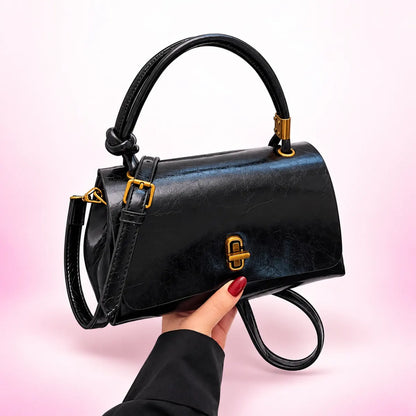 Black flap satchel with curved top handle, shoulder strap and gold-tone clasp
